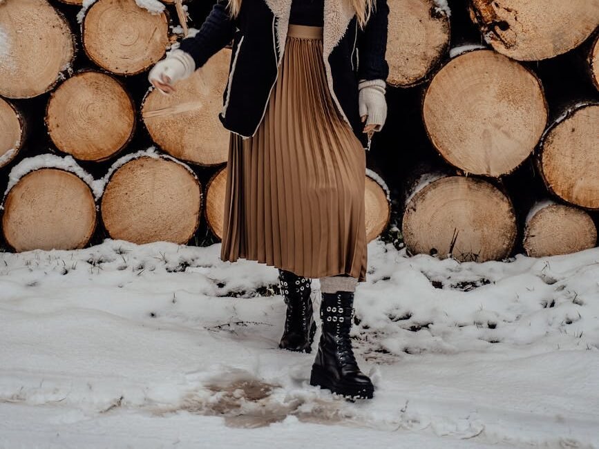 a woman in brown skirt standing near the chopped woods on a snow covered ground